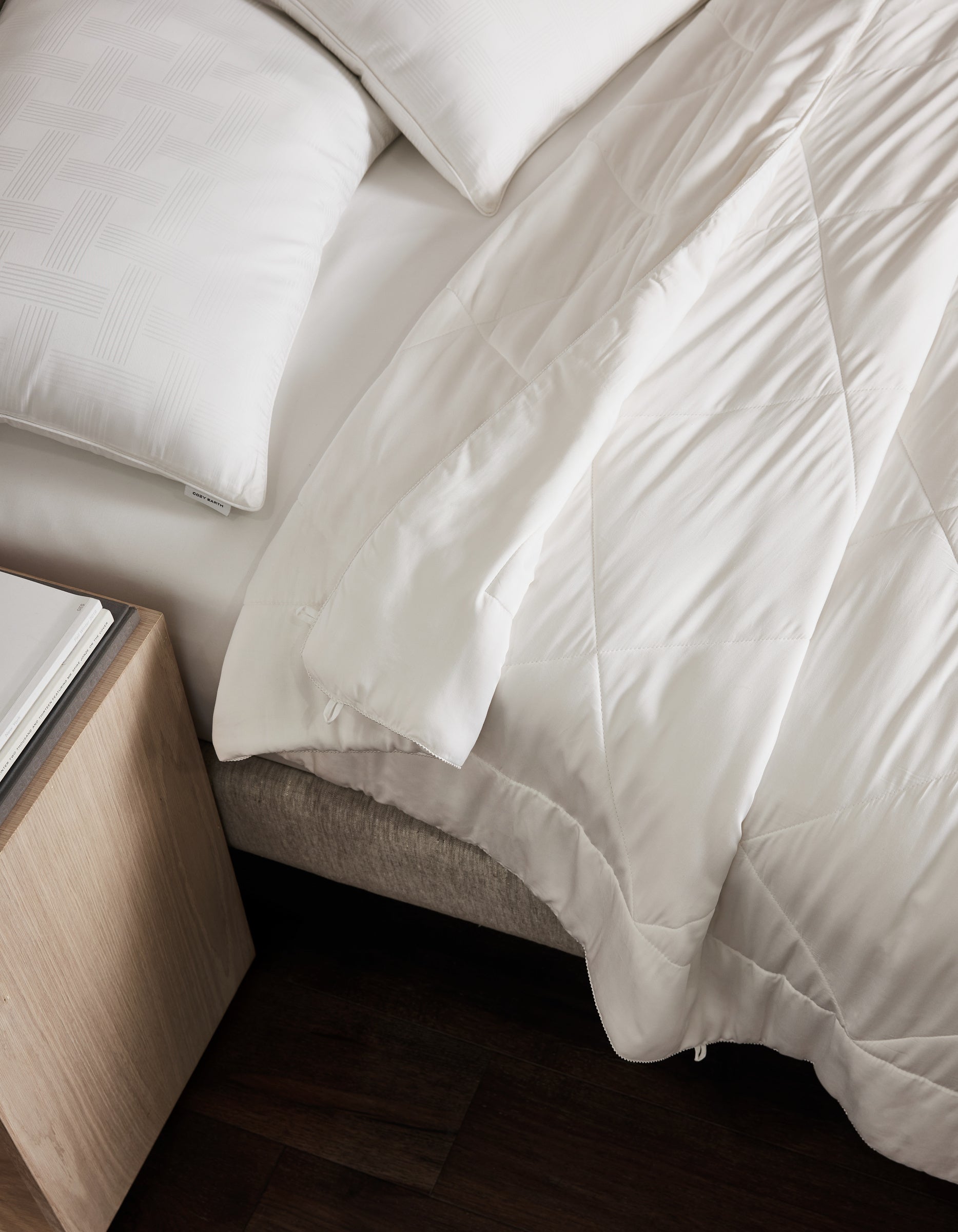 A neatly made bed features white pillows and the Cozy Earth Bamboo Viscose Comforter, partially folded back. Beside it, a light wood nightstand with a book rests on dark wood floors.|Filling:Standard